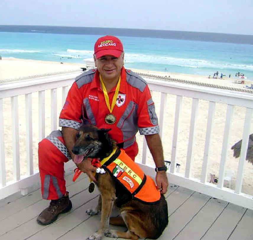 Rodolfo Núñez Renault, con uniforme de rescate y medalla, junto a su perro de rescate en un balcón frente al mar de Cancún